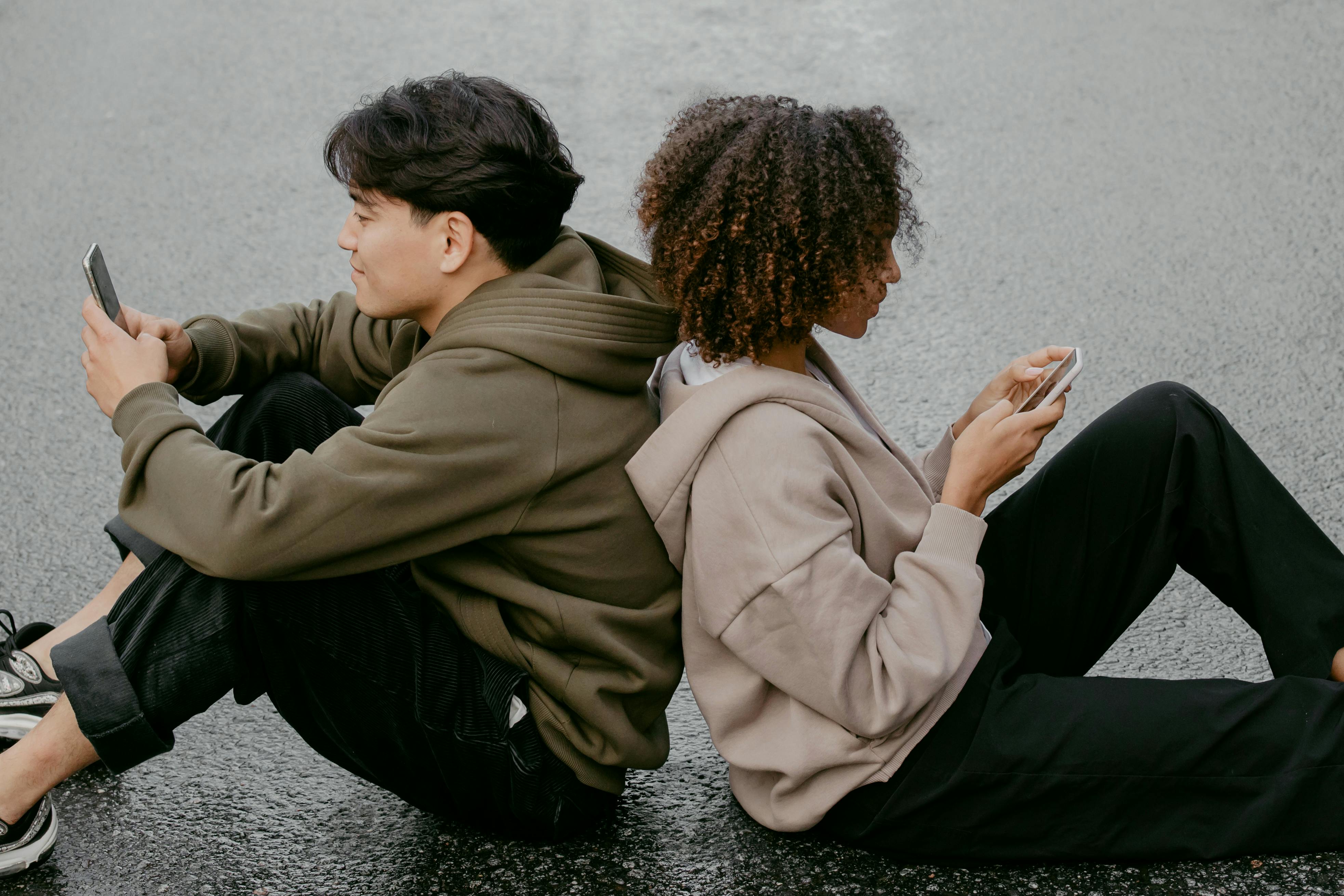 girl and boy in long distance relationship sitting back to back on their phone